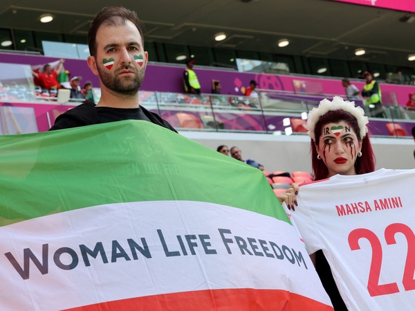 An Iran supporter with blood tears makeup on her face holds a jersey with the name of Mahsa Amini with another supporter holding a flag reading "Woman life freedom" as they attend the match between Wales and Iran.