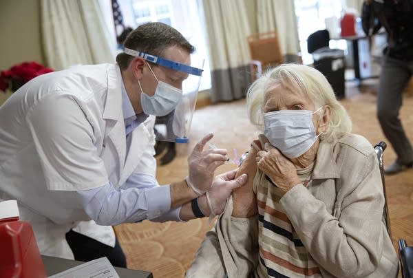 A man wearing PPE uses a needle to inject a women with a vaccine. 