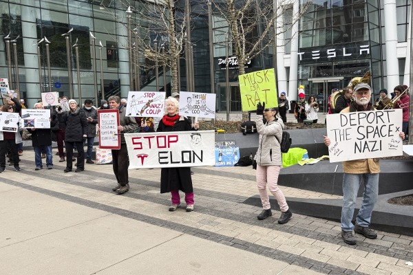 Protesters holding signs rally outside a Tesla store in Boston. One sign says "Stop Elon." 