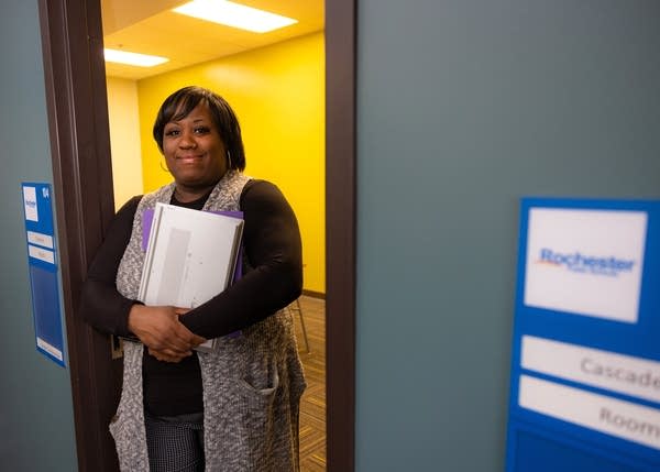 A woman poses with a binder in her arms, standing in a doorway.