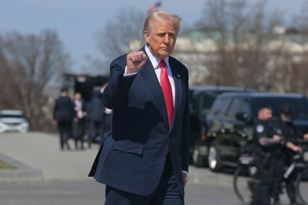 In this photo, President Trump is walking outdoors with his right fist raised to about shoulder height. He's wearing a dark blue suit and red tie.