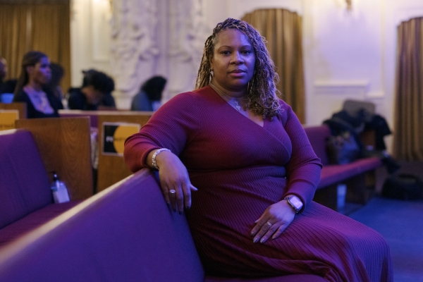 Dr. Lena Green wears a maroon dress and sits in a church pew for this portrait. 