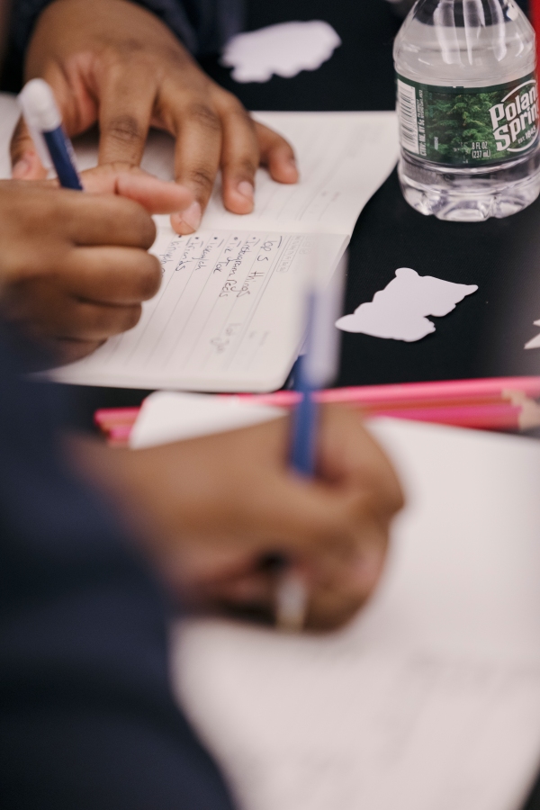 The photo shows a close up of students' hands as they write in notebooks. 