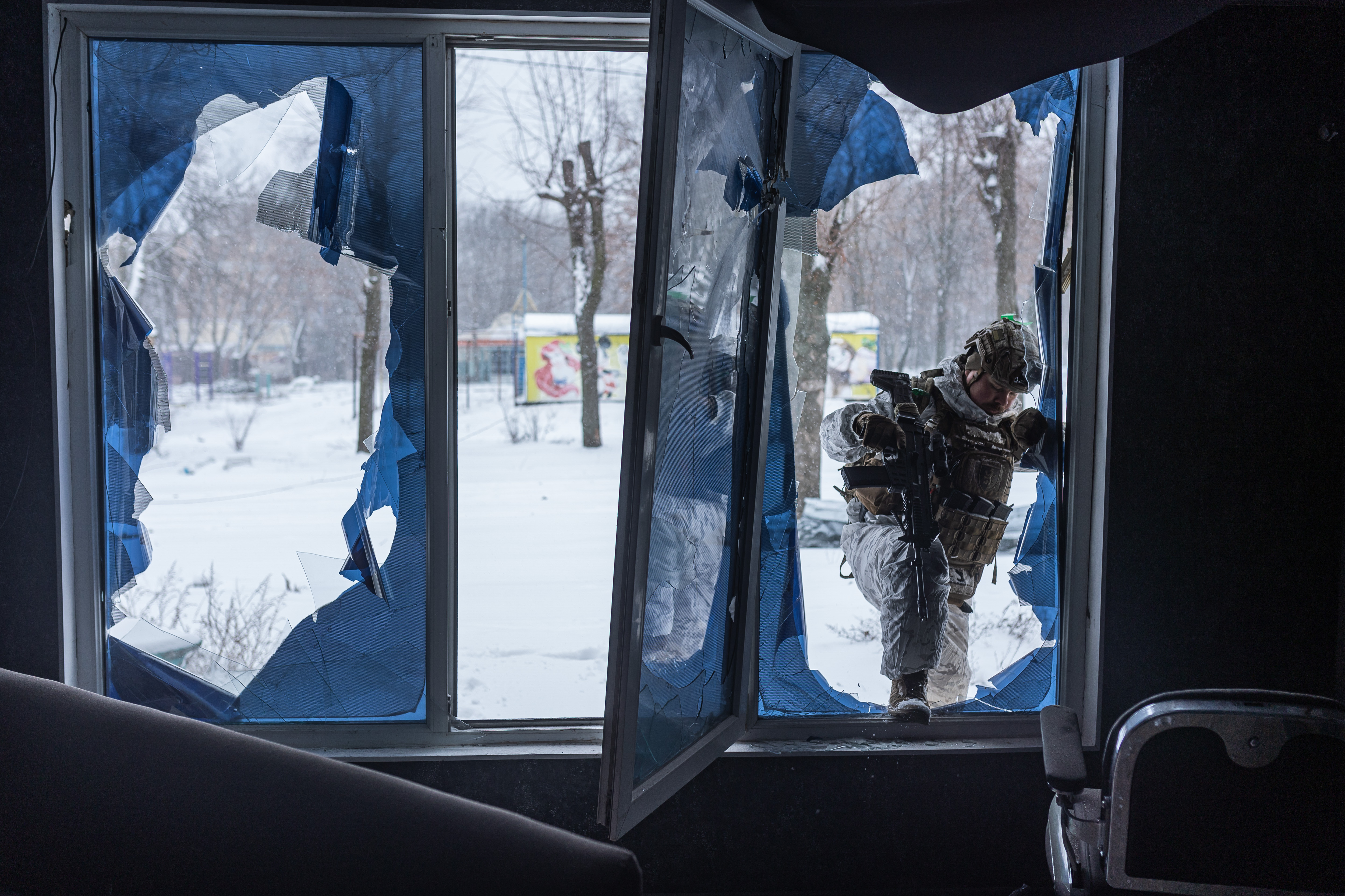 A service member enters a building where a window has been destroyed.