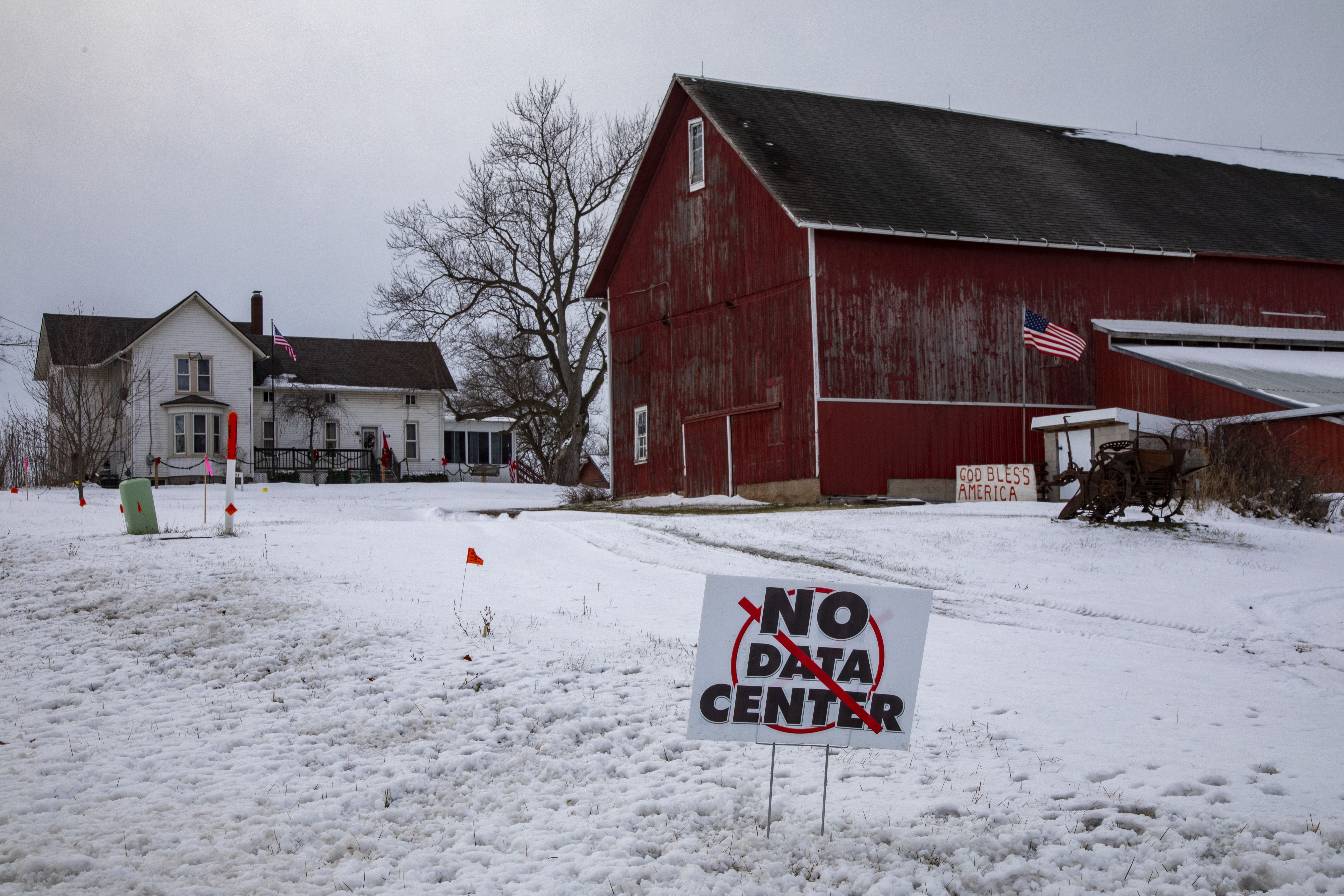 A sign that reads No Data Center sits on a snowy lawn in front of a farm