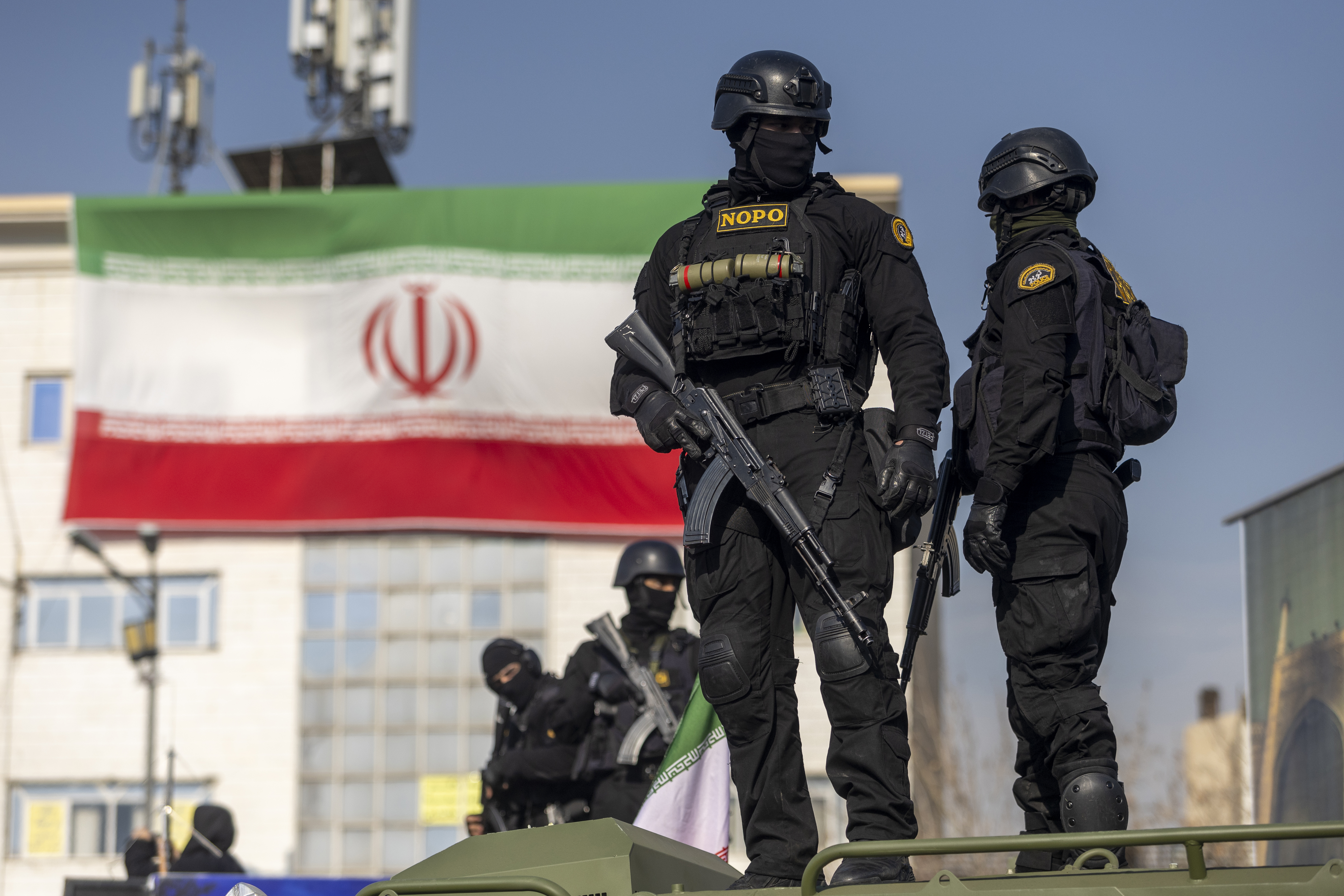 Security forces standing in front of the Iranian flag