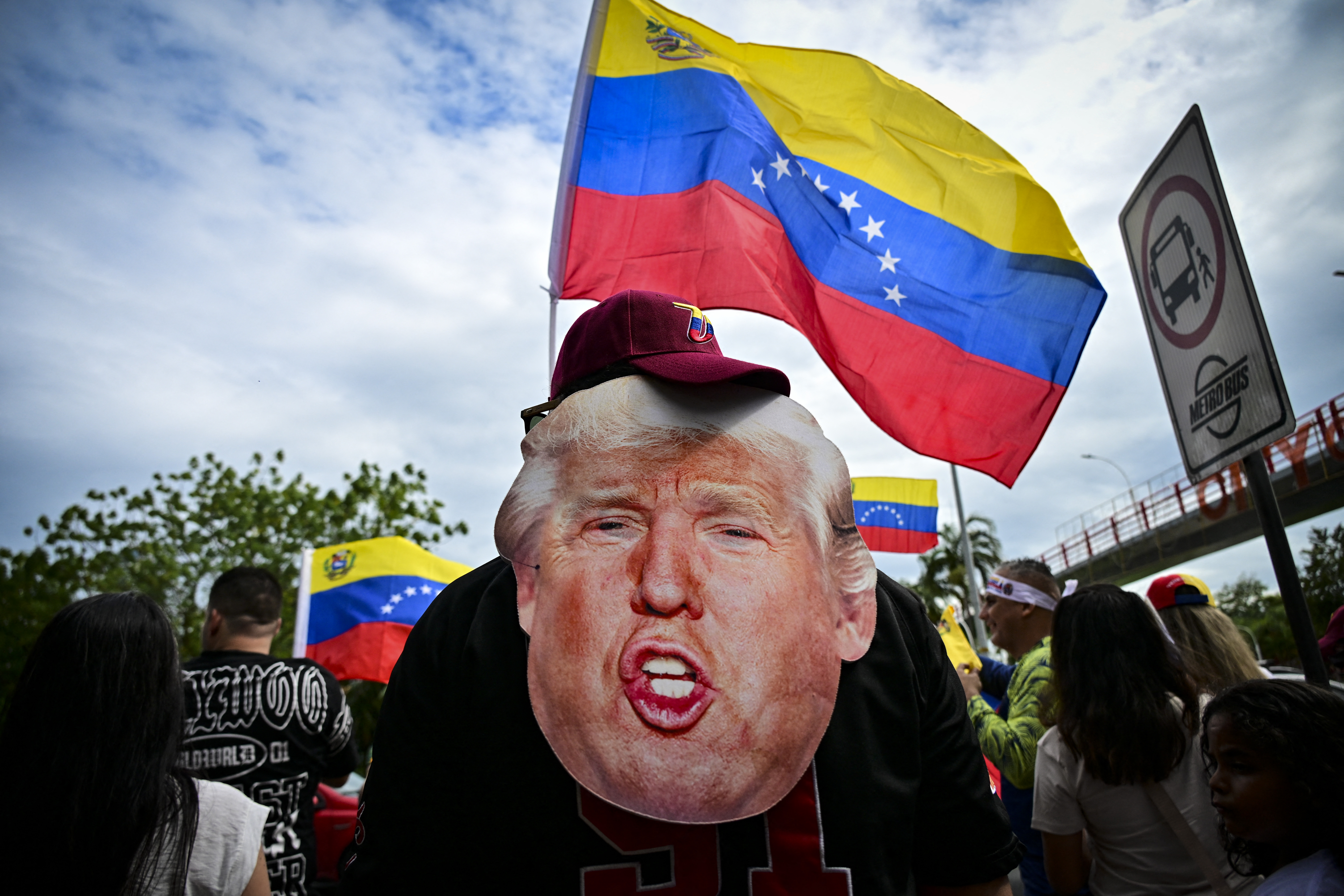 Man holds a Trump mask in front of a Venezuelan flag