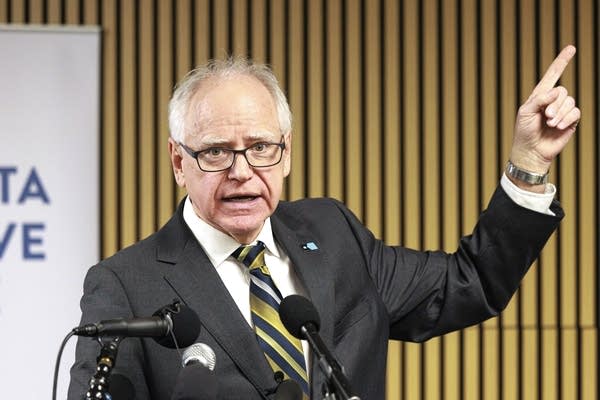 Gov. Tim Walz stands behind a podium with a number of microphones.