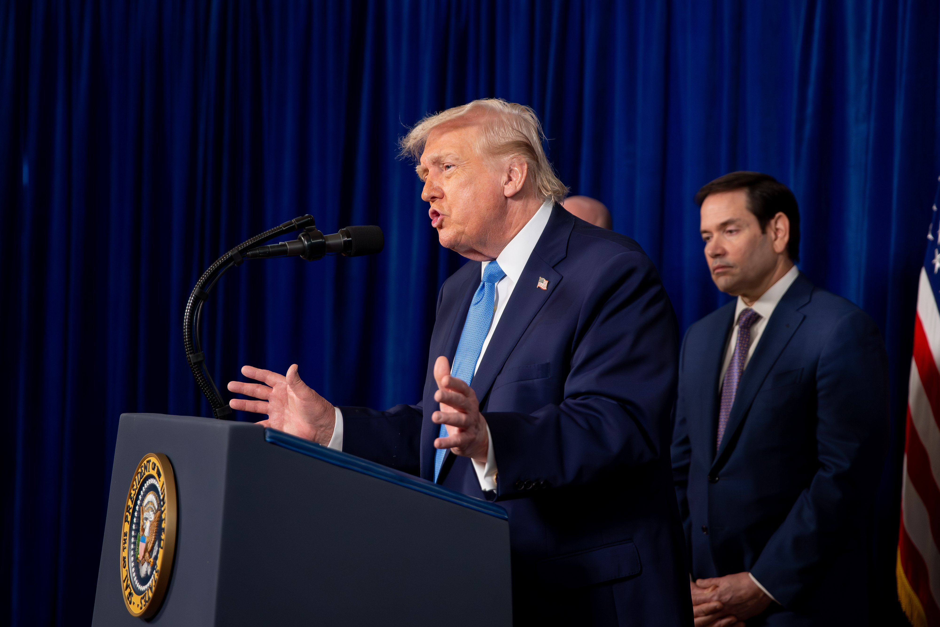 Trump speaks at a lectern with Rubio behind him. 