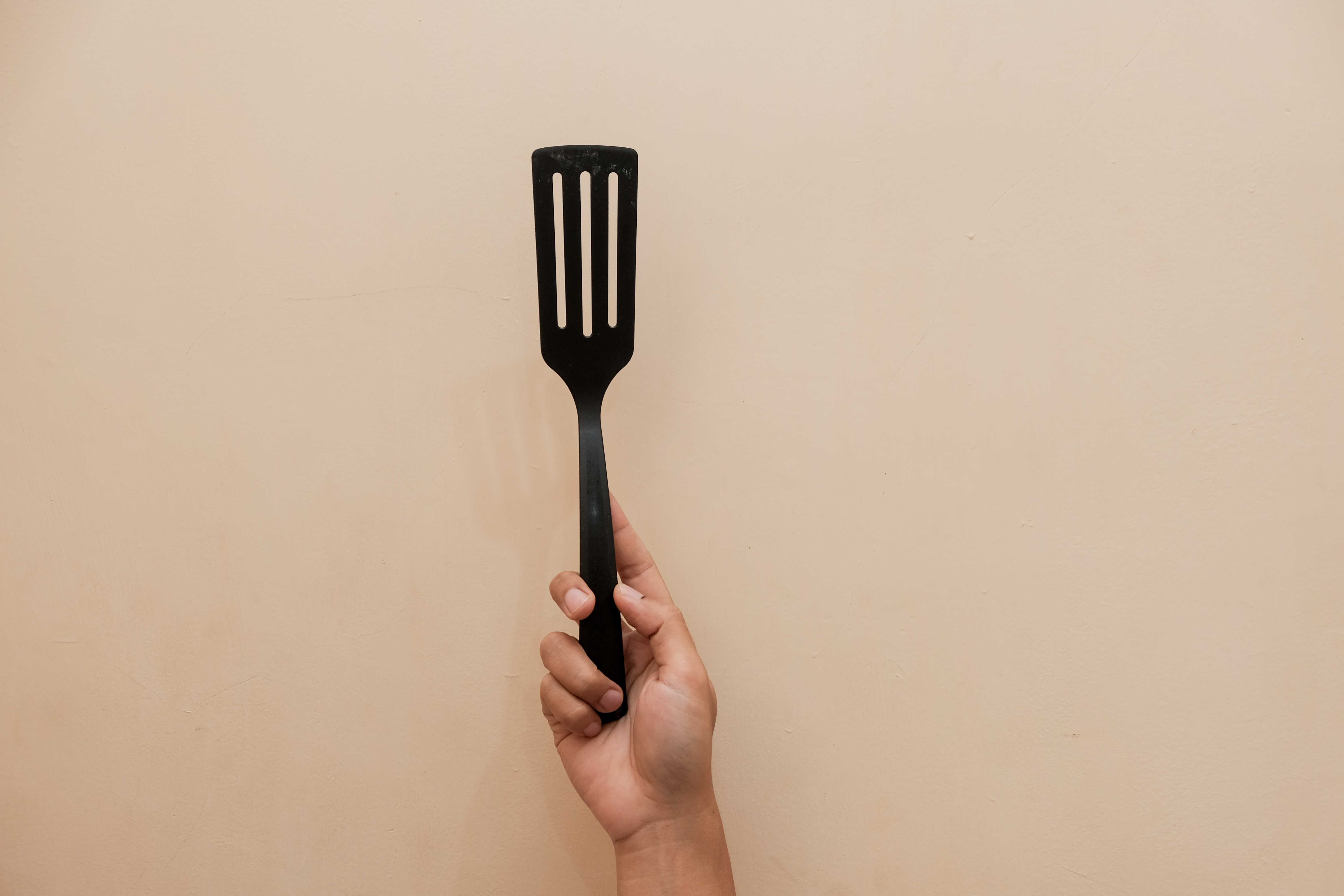 Closeup of a hand holding a black plastic spatula for a frying pan.