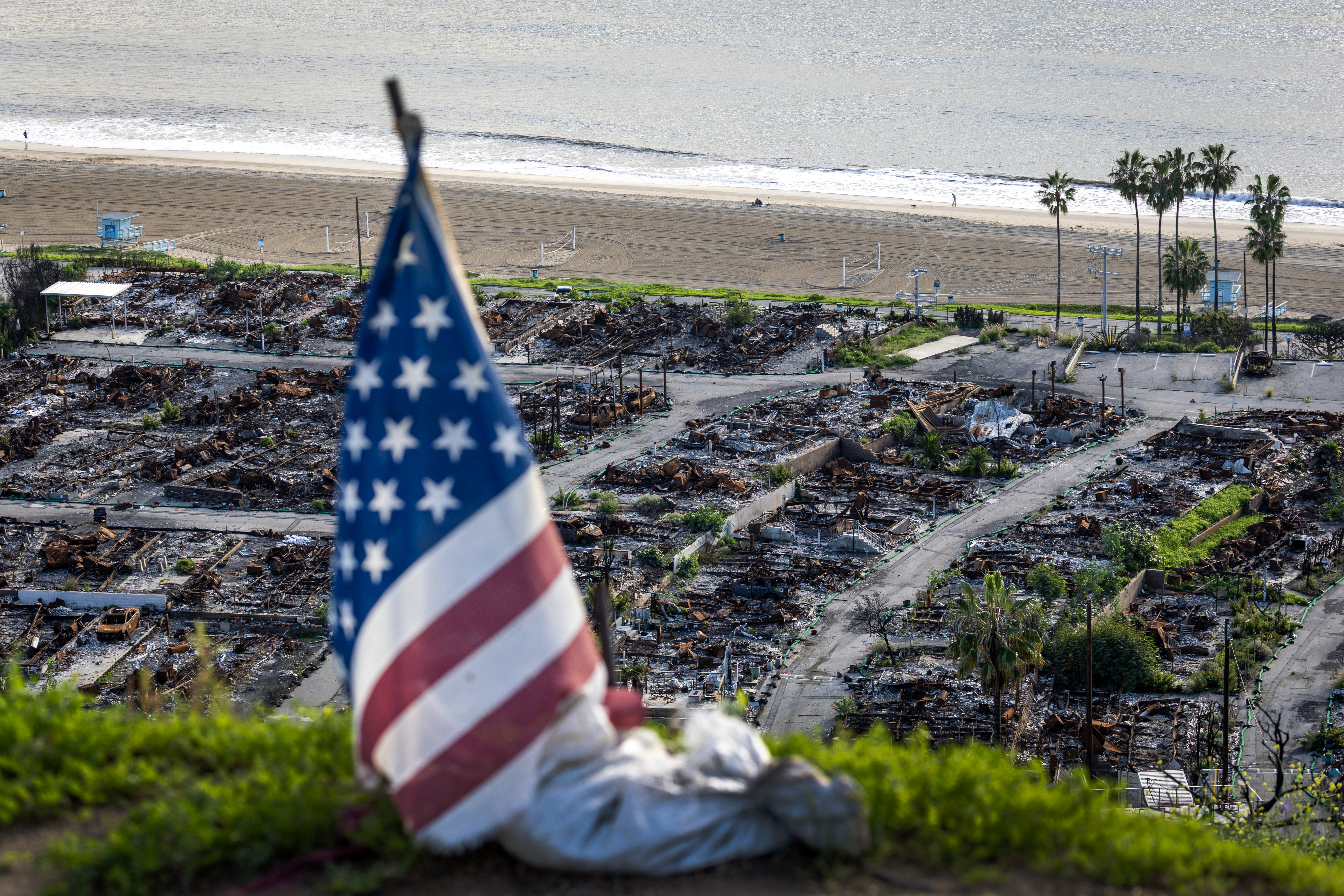 An American flag and sand bag stands on a cliff overlooking the remains of the Pacific Palisades Bowl Mobile Estates, which was destroyed in the 2025 Palisades fire. An American flag and sand bag stands on a cliff overlooking the remains of the Pacific Palisades Bowl Mobile Estates, which was destroyed in the 2025 Palisades fire.