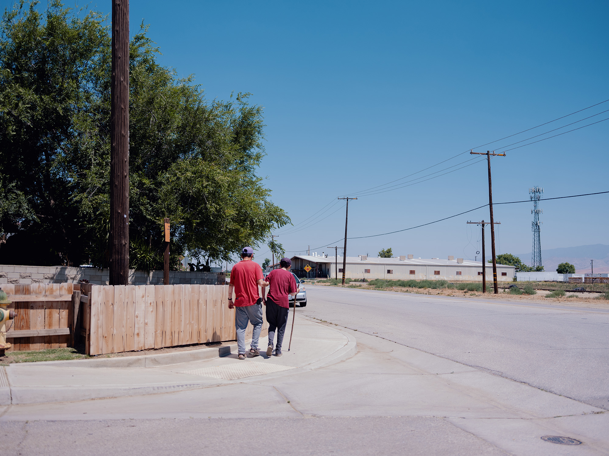 Two men walk down a sidewalk in a rural town.