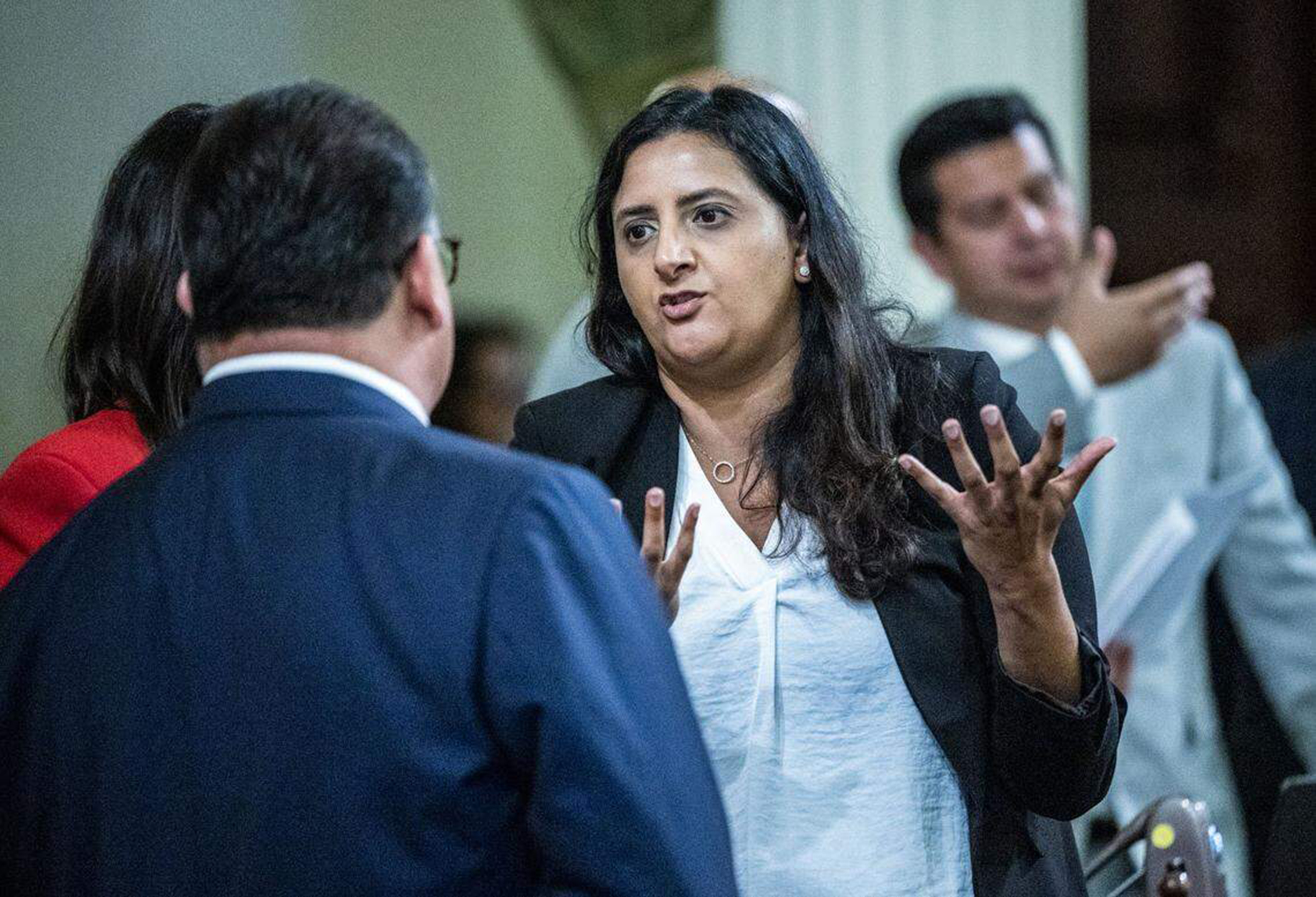 A woman, holding her hands in front of her with the palms facing up, speaks to a man, whose back faces the camera.