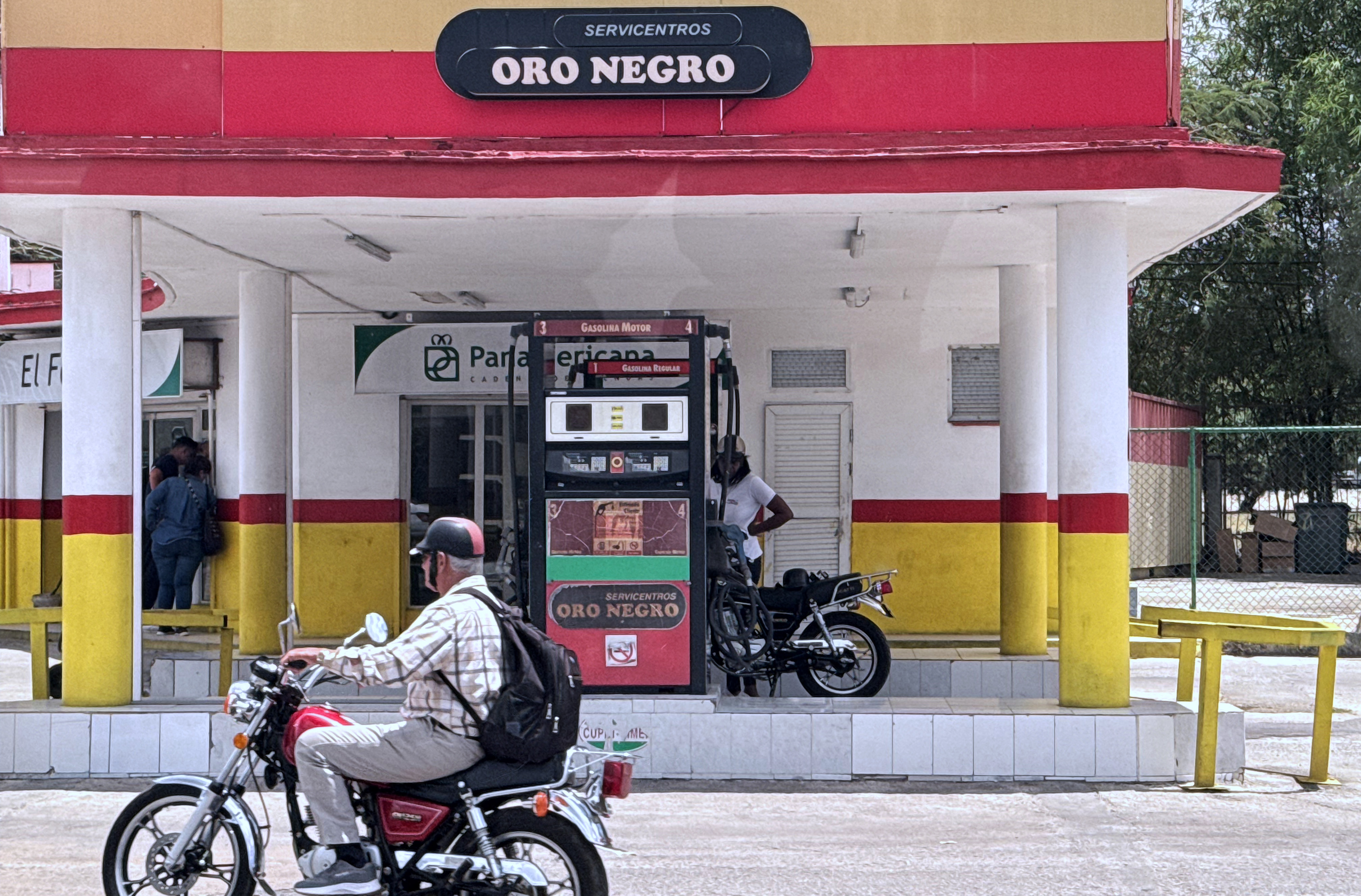A man on a motorcycle rides by a gas station in Havana, Cuba.