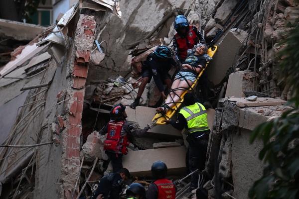 Rescue workers carry a person on a stretcher out of a collapsed building.
