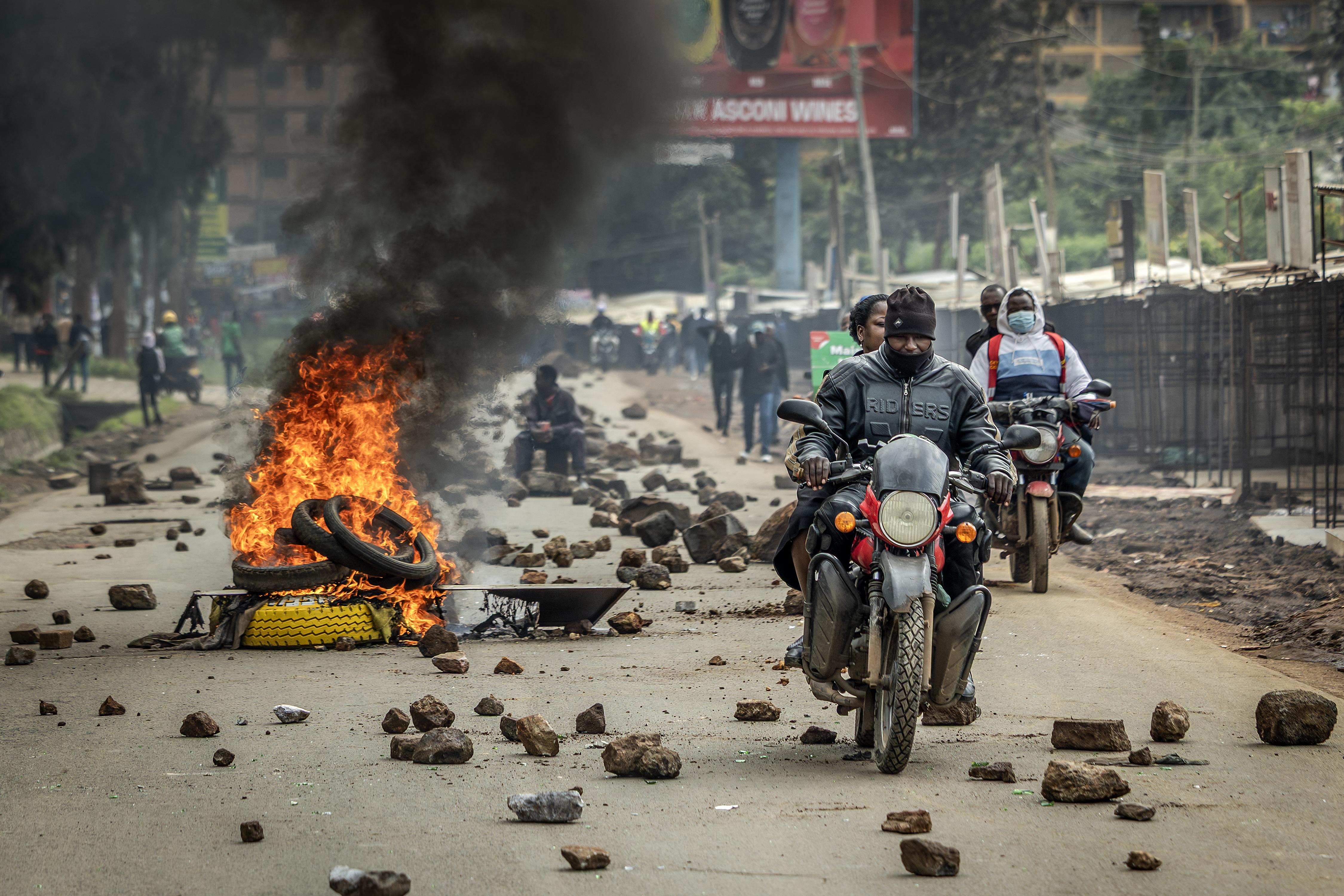 A motorcycle driving past a flaming barricade. 