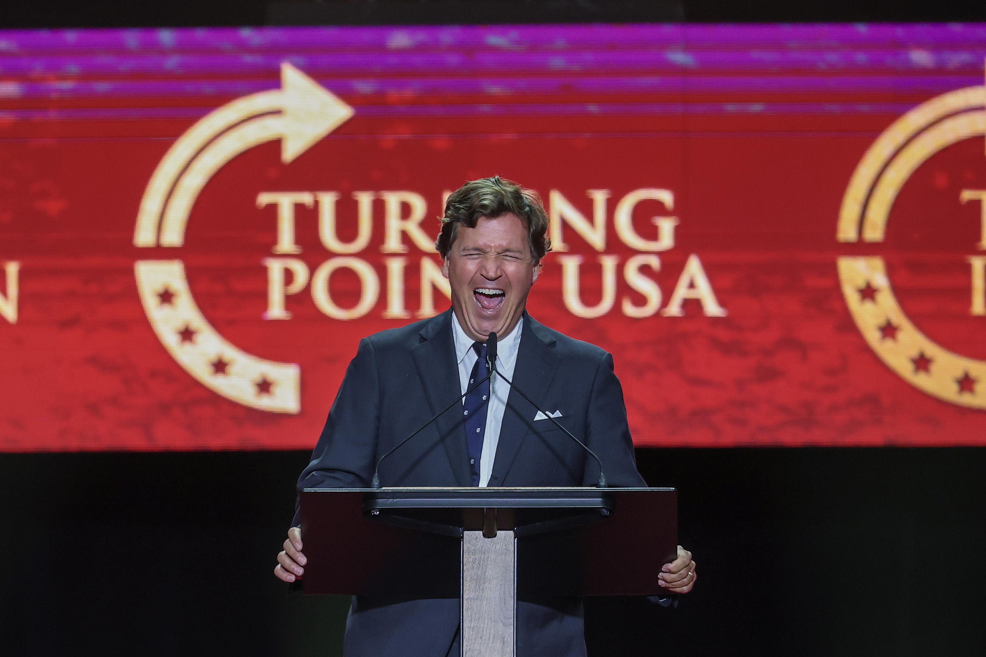 Tucker Carlson at a podium for a TPUSA event