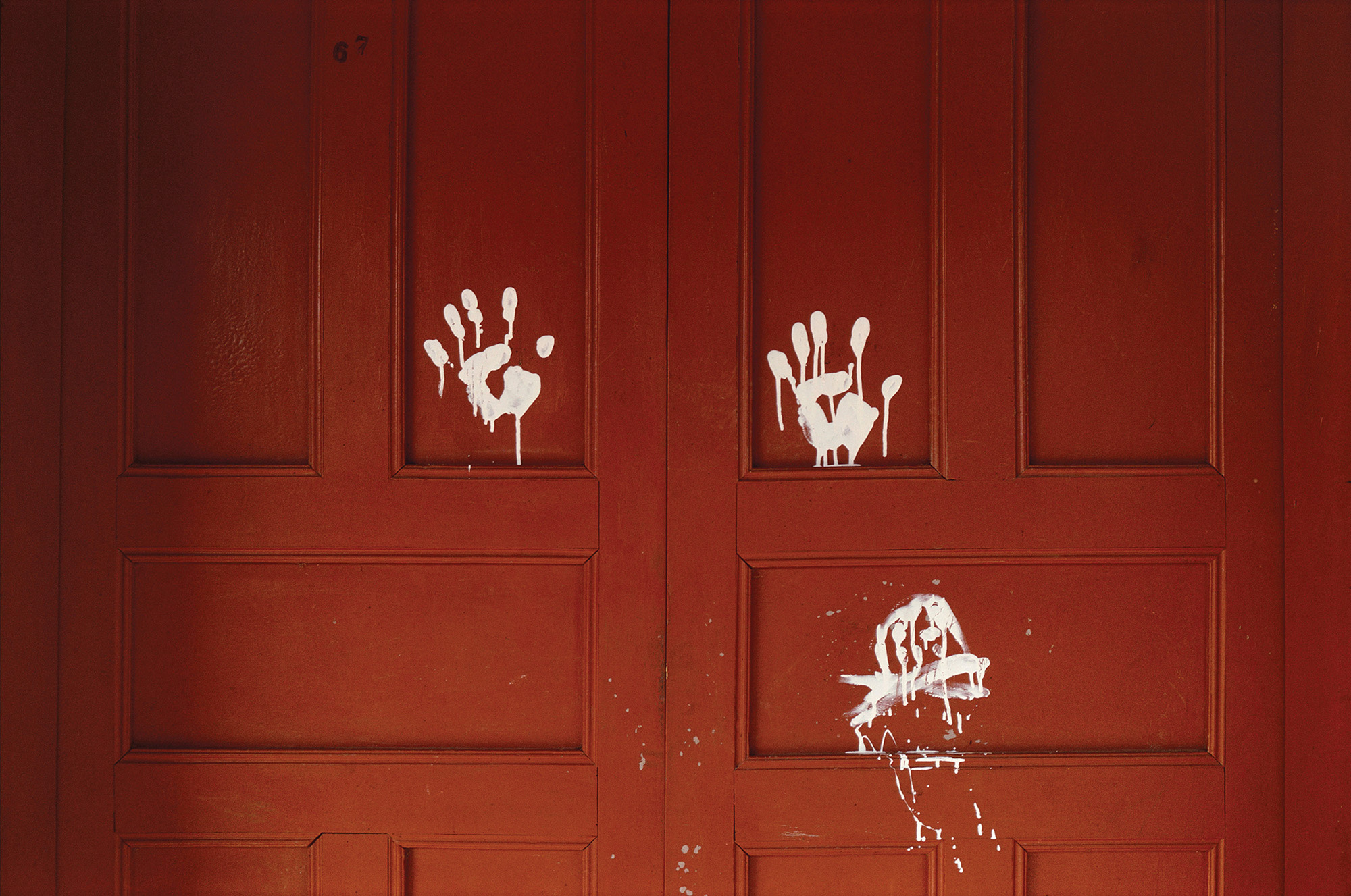 Two white handprints and a crude skull and crossbones are painted on a red door.
