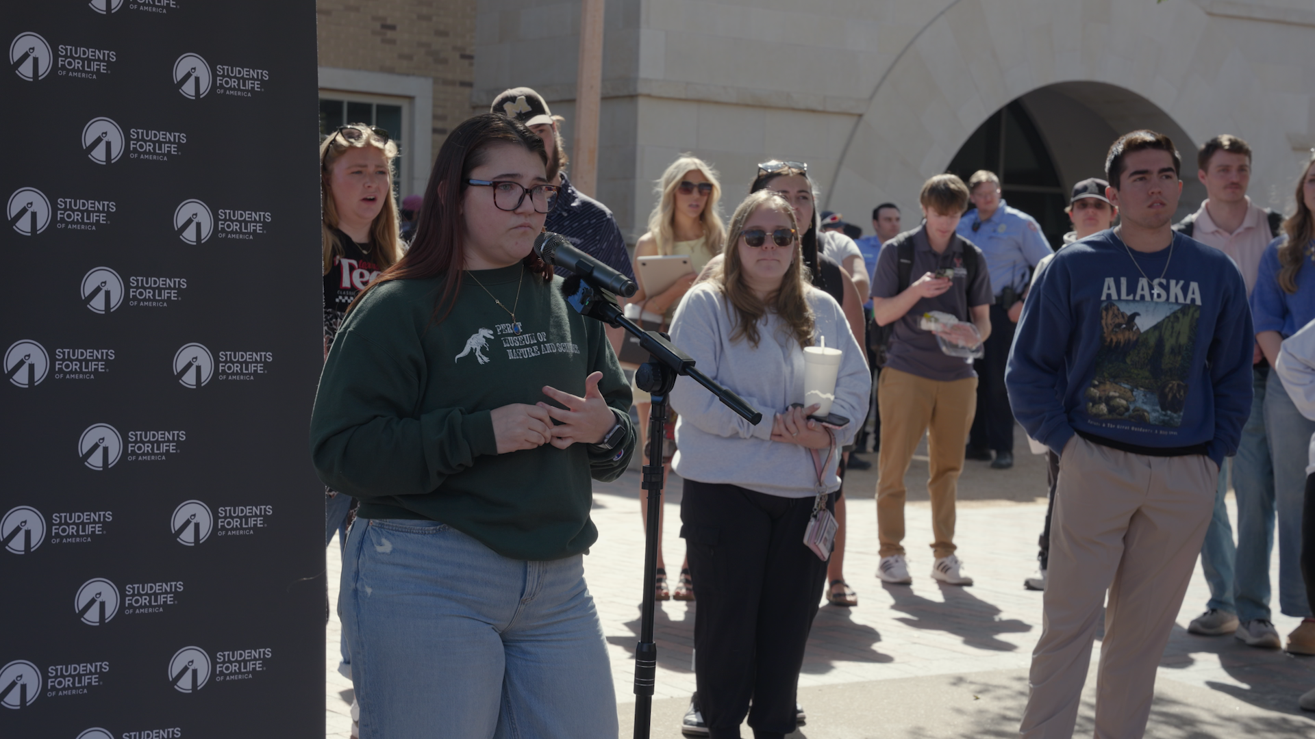 A young woman stands in front of a microphone during a debate on campus with Kristan Hawkins