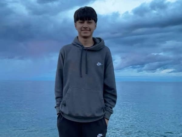 A boy stands on rocks at the edge of water on a cloudy day.