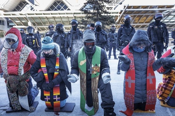 A group of clergy kneel outside the airport.