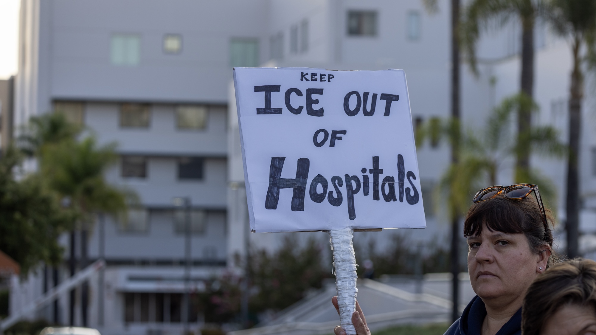 A woman holds a sign saying “Keep ICE out of hospitals” at a protest in front of Glendale Memorial Hospital.