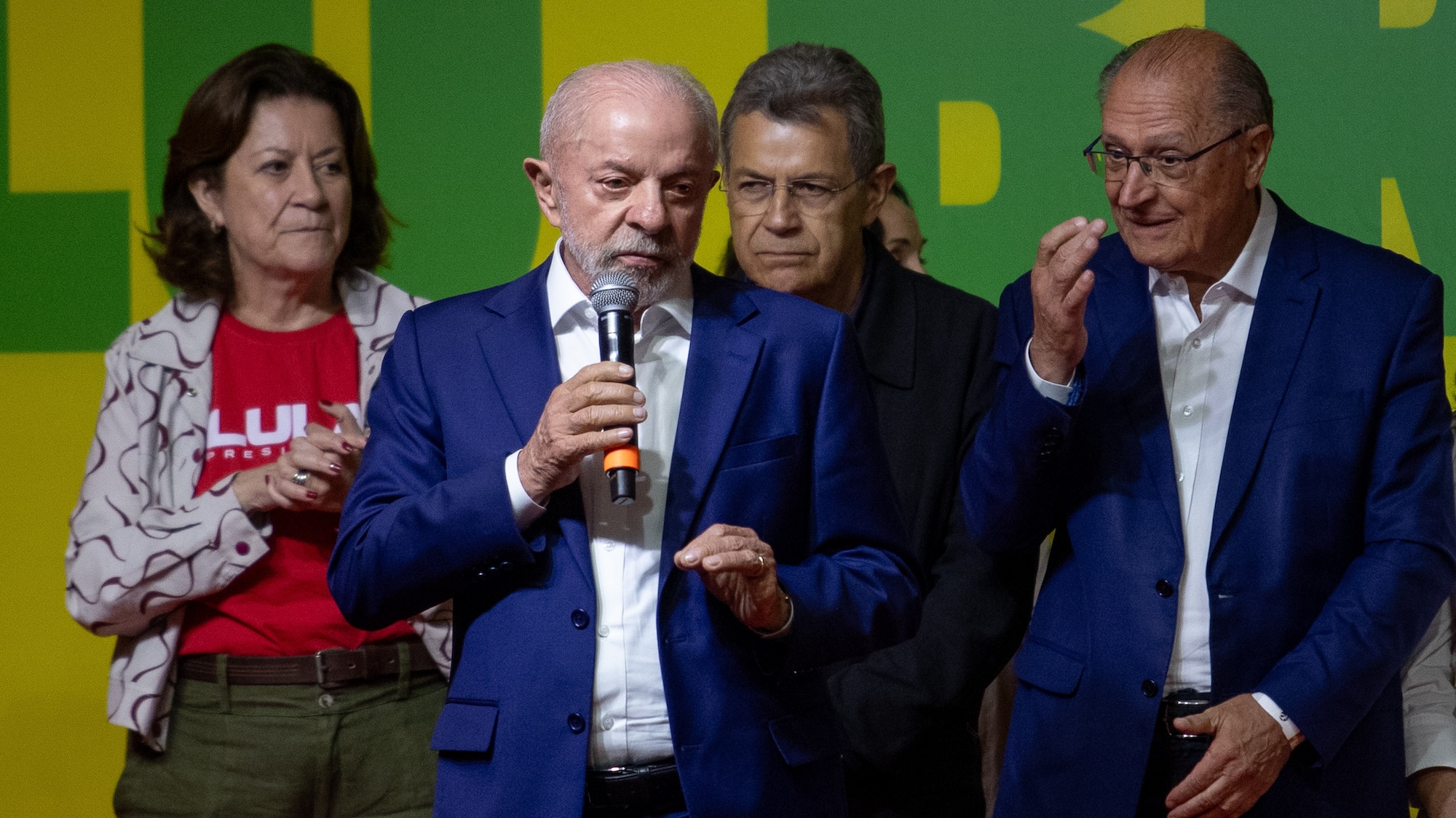 Brazil's president, wearing a blue blazer and a white buttondown, addresses the crowd, speaking through a microphone. 