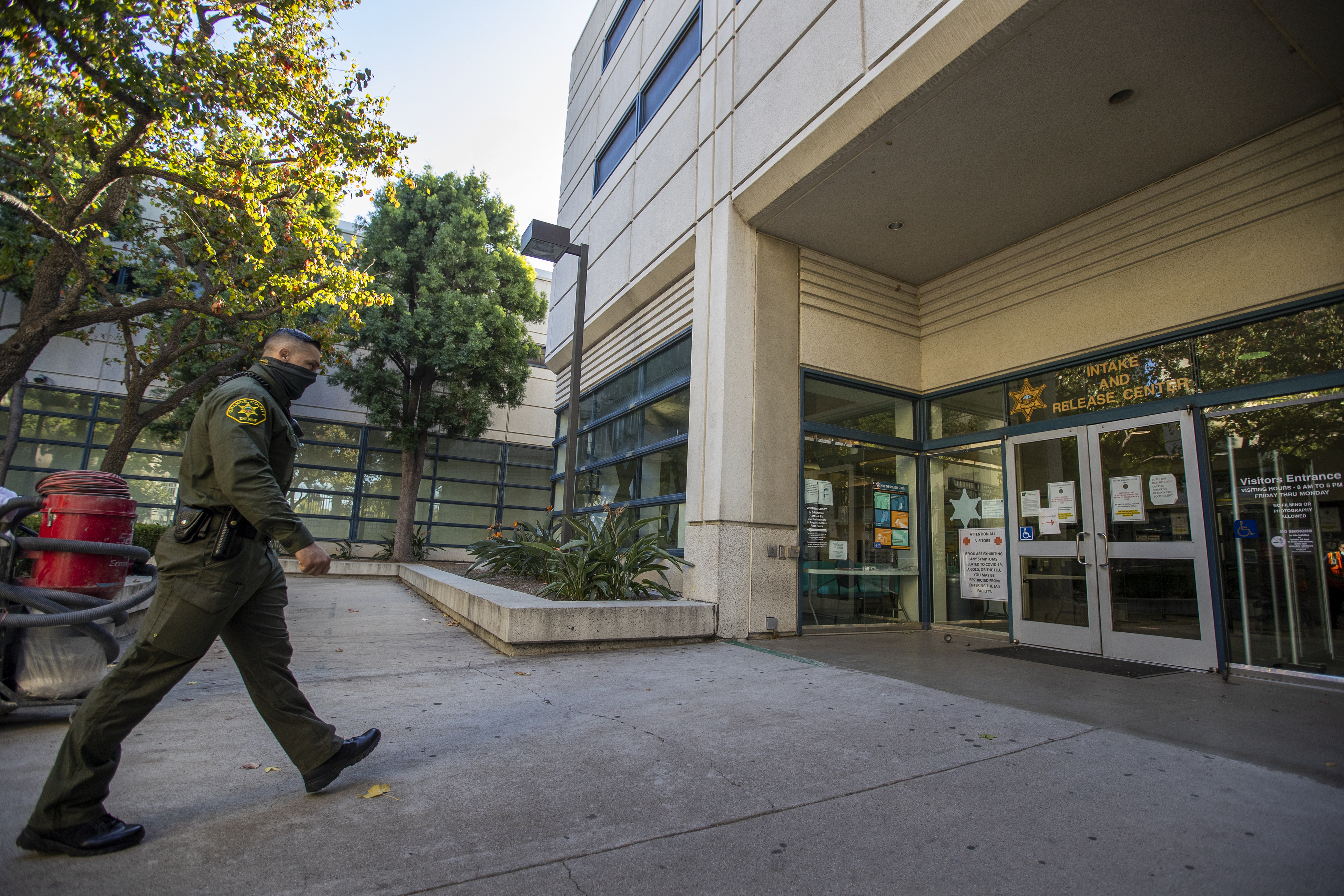 A photograph of a sheriff deputy walking toward the entrance doors of a building that has signage that reads "Intake and Release Center"