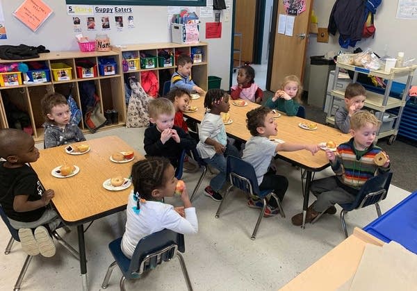 Children sit around tables.