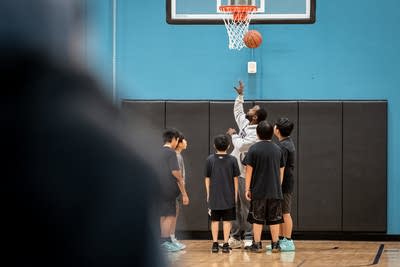 A basketball coach shoots a layup next to a group of boys.