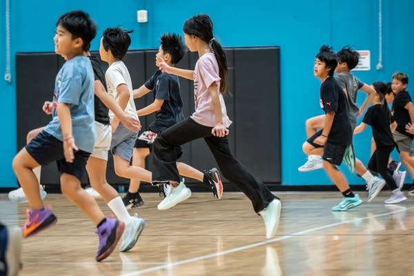 Children raise their knees as they run across a basketball court.