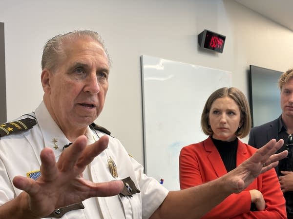 A law enforcement officer raises his hands while speaking to reporters.
