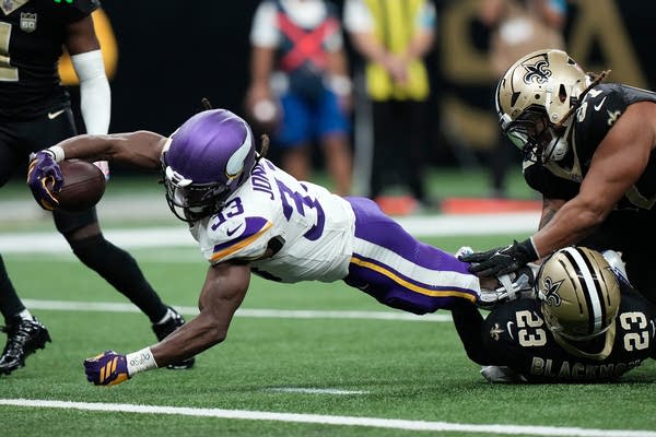 A Vikings football player dives and reaches out with the ball in-hand to score while being tackled.