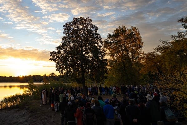 A crowd of people stand on a beach at sunrise