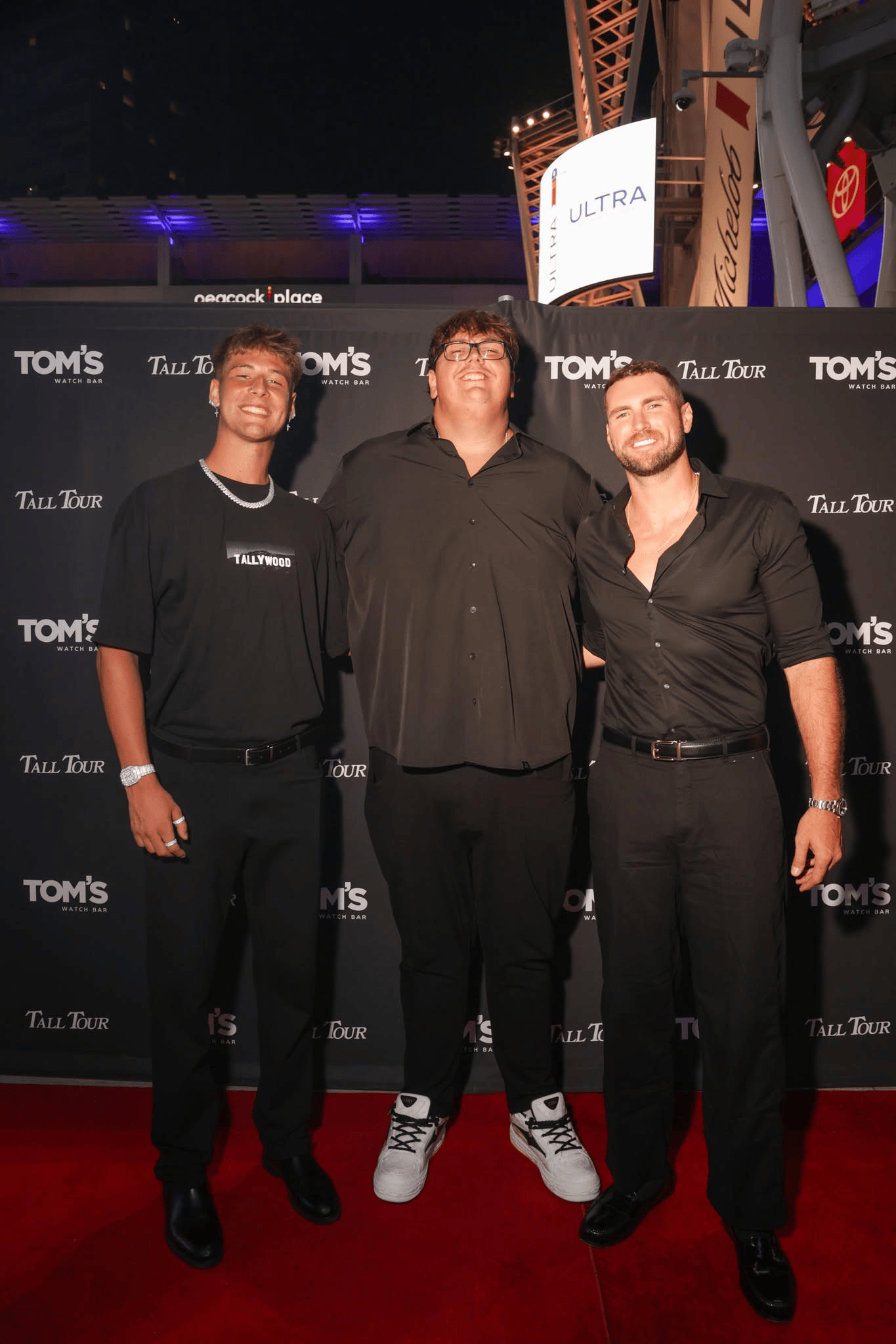 Men in black smile on red carpet