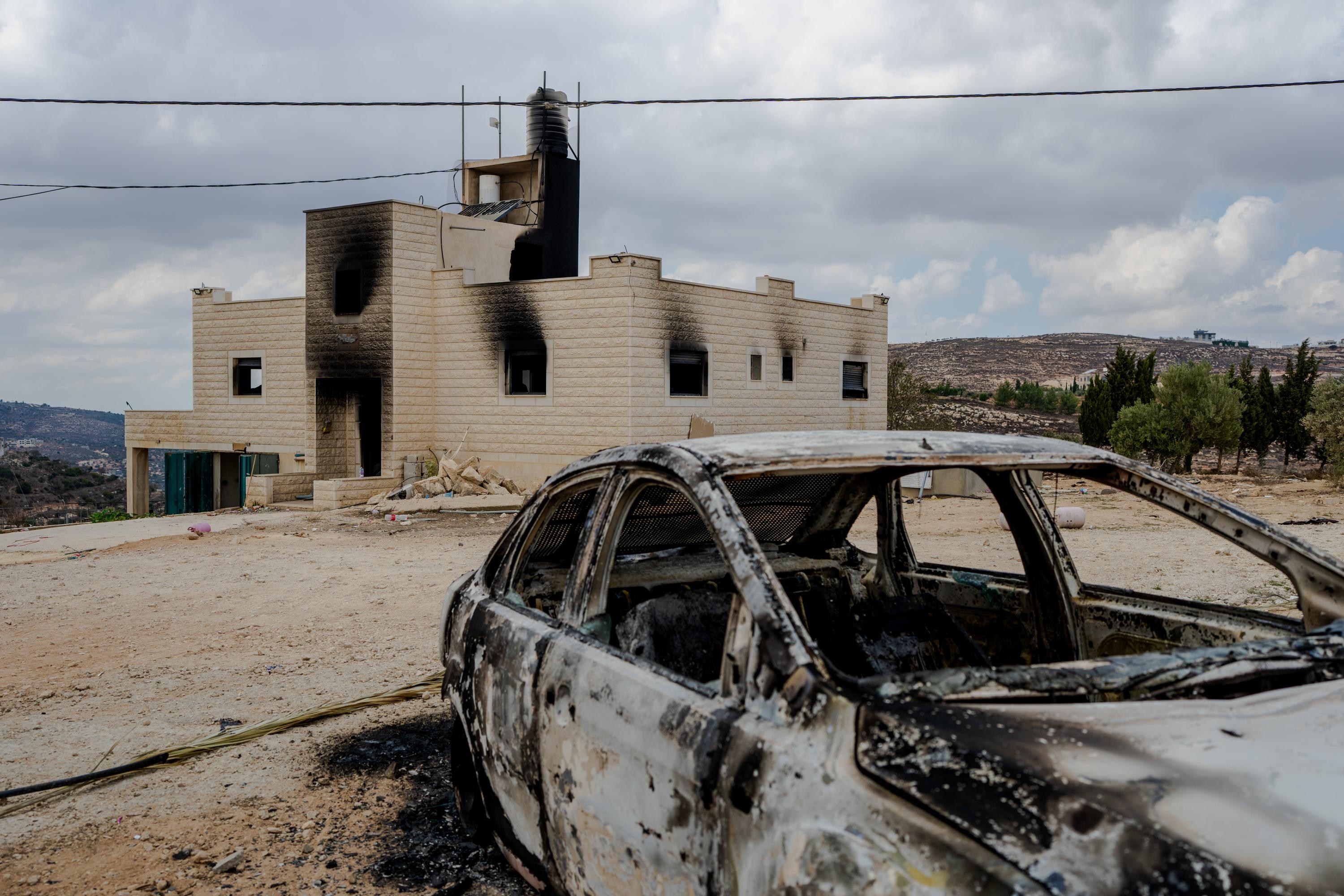 A burned-out car sits in front of a soot-smeared, burned house in the West Bank.