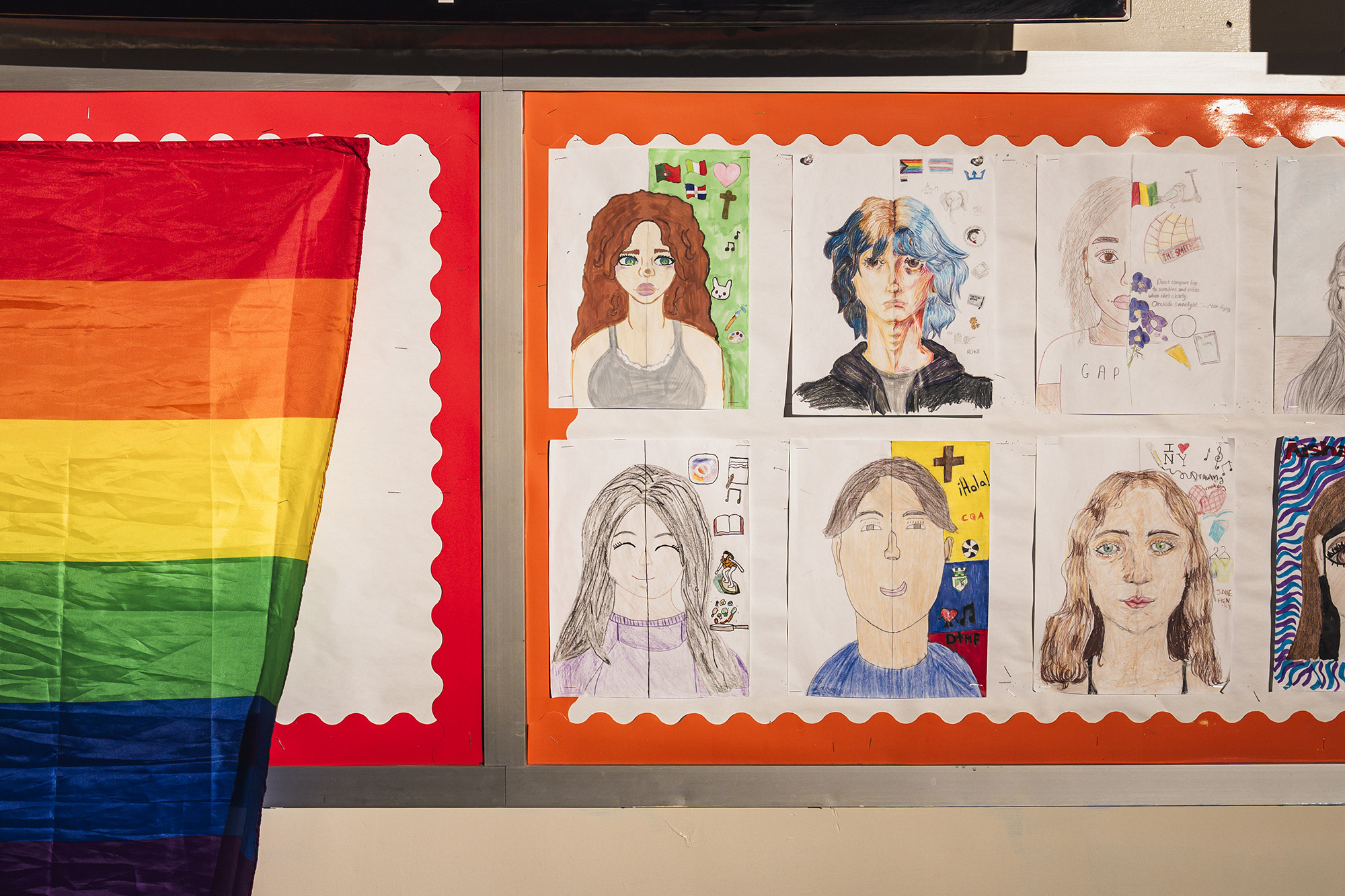 Student self-portraits next to a pride flag in a classroom.