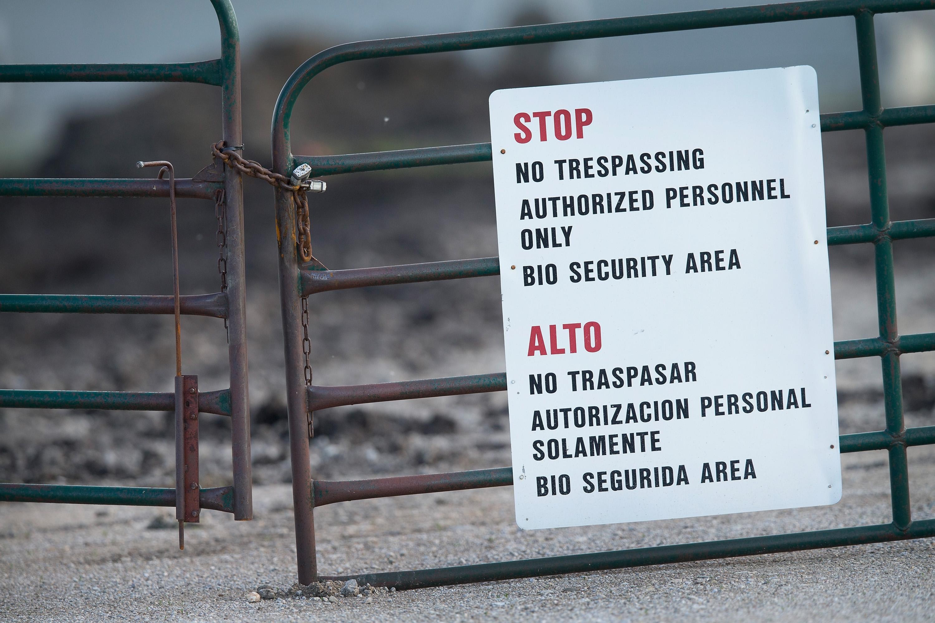 A sign attached to a farm gate reads “Stop. No trespassing. Authorized personnel only. Bio security area.”